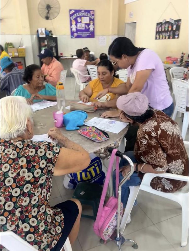 Una técnica acompaña a un grupo de adultos mayores durante una actividad de lectura y escritura